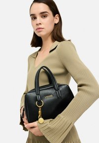 Sac à main en cuir noir texturé avec une forme structurée, des accents en métal doré et un détail de porte-clés. Logo "LIUJO" embossé à l'avant.