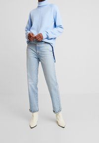 Sudadera azul claro con cuello alto, corte relajado y textura acanalada, combinada con jeans rectos azul claro y botines tobilleros en color blanco roto.