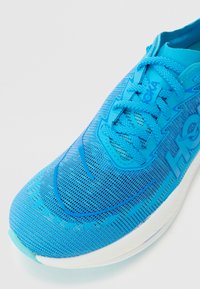 Blue running shoe with mesh upper, curved shape, textured surface, pronounced laces, and white midsole detailing.
