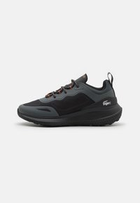 Chaussure de sport noire avec des accents gris, une tige en mesh texturé, des lacets orange contrastants et une semelle en caoutchouc épaisse dotée d'un motif de crampons.