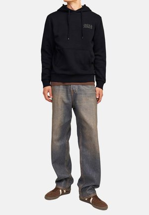 Black hoodie with a front kangaroo pocket and drawstrings. Paired with faded blue wide-leg jeans and brown sneakers.