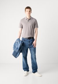 Szürke pólóing fehér részletekkel, laza kék farmernadrággal és farmerdzsekivel. A szettet fehér sportcipők és fekete öv egészíti ki.