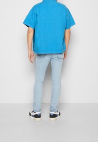 Camicia azzurra a maniche corte realizzata in tessuto leggero, abbinata a jeans slim-fit azzurri e sneakers nere con accenti bianchi.
