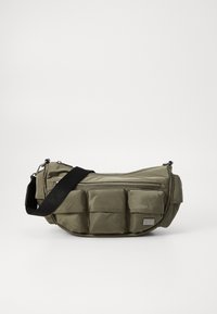 Sac bandoulière en nylon vert olive avec une finition texturée, comprenant un zip sur le dessus, plusieurs poches avant et une bandoulière réglable.