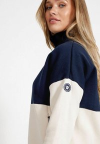 Färgfältad fleece sweatshirts med en marinblå övre halva och en krämfärgad undre halva, med hög krage och en märkespatch på ärmen.