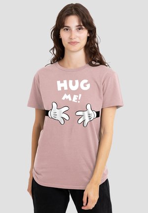 Helles pinkes T-Shirt mit einem Grafikdruck von weißen Händen, die nach außen strecken, und dem Text "UMARME MICH!" in fetten weißen Buchstaben. Weicher Stoff mit angenehmer Textur.