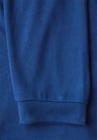 Blått stickat tyg med ett strukturerat mönster, med en ribbad mudd synlig i botten, vilket visar flexibilitet och mjukhet.