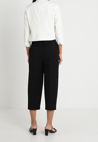 Bílé zkrácené sako s třičtvrtinovými rukávy, které je kombinováno s černými vysokými kalhotami culottes. Obě části mají hladkou texturu a minimalistický design.