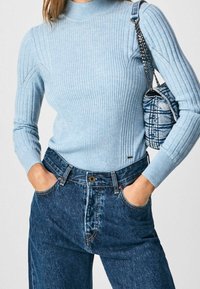 Pull à col roulé côtelé bleu clair avec des manches longues, associé à un jean en denim bleu taille haute. Sac circulaire au motif denim.