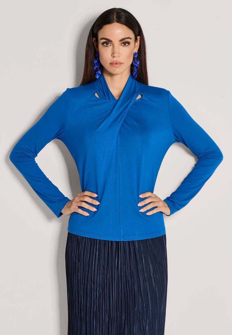 Blaues Langarmoberteil mit einem einzigartigen Drapierungs-Ausschnitt und Cut-out-Details. Weicher Stoff, figurbetontes Design, kombiniert mit einem plissierten marineblauen Rock.