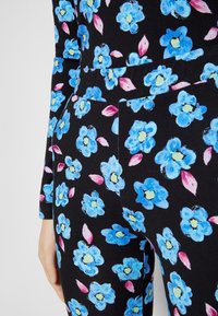 Tela negra con un estampado floral que presenta flores azules y hojas rosas. El diseño es vibrante, con una textura suave y una forma ajustada.