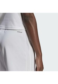 Pantalons de sport blancs au design épuré, arborant le logo "AEROREADY" sur le côté. Texture lisse, style minimaliste et sans motifs visibles.