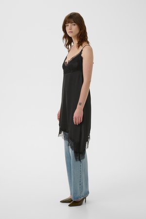Schwarzes Seiden-Nachthemd mit Spitzenbesatz am Saum und am Ausschnitt, ausgestattet mit dünnen Trägern und einer lockeren Passform, kombiniert mit hellblauen Jeans mit geradem Bein.