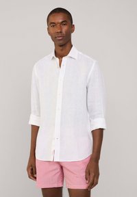 Witte linnen blouse met lange mouwen, knoopsluiting bij de manchetten, en een klassieke kraag, gecombineerd met rode en witte gestreepte shorts.