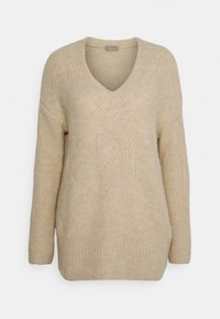 Beżowy sweter z dekoltem w serek, wykonany z teksturowanej tkaniny, zdobiony wzorami w warkocze oraz ściągaczami na mankietach i u dołu.