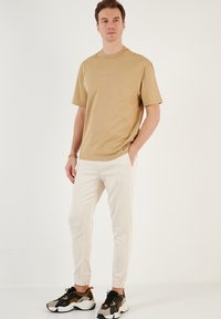 Beige bomuld t-shirt med korte ærmer og rund hals, parret med hvide joggerbukser og sorte sneakers med orange detaljer.