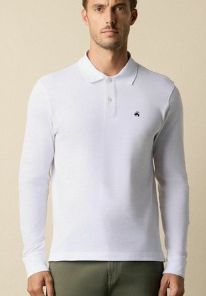 Bílá polokošile s dlouhým rukávem vyrobená z měkké tkaniny, s límečkem a malým tmavým logem na hrudi. Jednoduchý design bez vzorů.