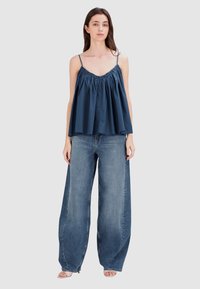 Navyblauwe katoenen mouwloze top met geplooid decolleté, gecombineerd met lichtblauwe denim jeans met wijde pijpen. Lichtgekleurde sandalen maken de outfit compleet.