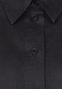 Chemise gris foncé à boutons, col pointu et quatre boutons noirs visibles sur le devant.
