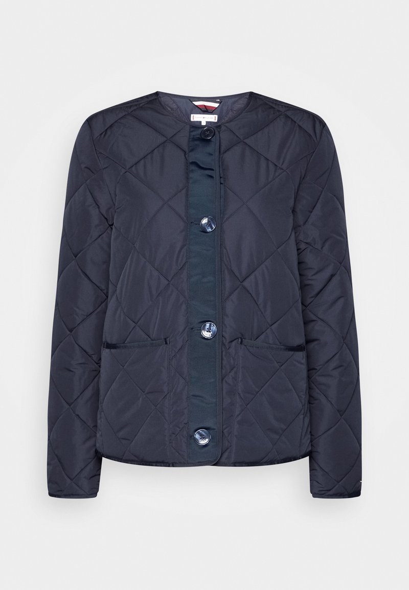 Chaqueta acolchada azul marino con cuello redondo, dos bolsillos frontales y botones grandes a lo largo del centro, que presenta una textura suave y un diseño ajustado.
