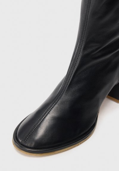 Schwarze Leder-Stiefelette mit runder Zehenpartie, glatter Textur, seitlicher Naht und klobigem Absatz. Gummisohle mit leichtem Kontrast.