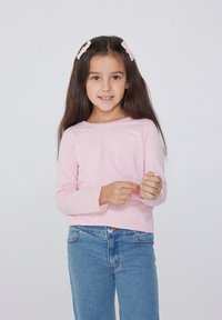 Světle růžová košile s dlouhým rukávem vyrobená z měkké látky, kombinovaná s modrými džíny. Košile má kulatý výstřih a přiléhavé rukávy.