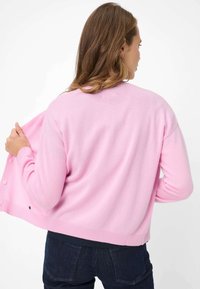 Cardigan rosa chiaro realizzato con materiale morbido, con una vestibilità rilassata, scollo rotondo e chiusura con bottoni. Texture liscia notevole e design semplice.