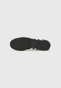 Semelle de chaussure de sport noire avec une surface texturée, présentant un motif géométrique et trois rayures blanches sur le côté.