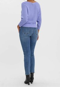 Pull en maille violet à manches trois-quarts, associé à un jean bleu taille haute et des bottines noires à talons, vu de dos.