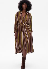 Koszulowa sukienka w paski w odcieniach brązu, zieleni i beżu. Posiada dopasowaną talię, zwiewną spódnicę z rozcięciem, długie rękawy oraz klasyczny kołnierzyk.