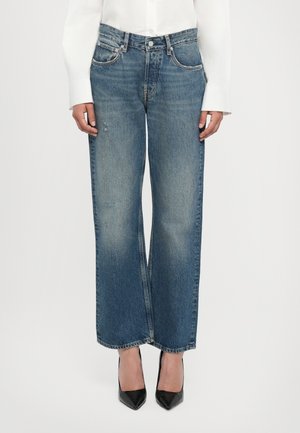 Blue denim wide-leg jeans with a faded finish, five pockets, and a buttoned waistband, paired with black pointed heels.