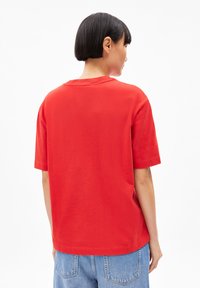 Rotes Baumwoll-T-Shirt mit lockerem Schnitt, kurzen Ärmeln und rundem Ausschnitt, das eine glatte Textur und ein einfaches Design aufweist.