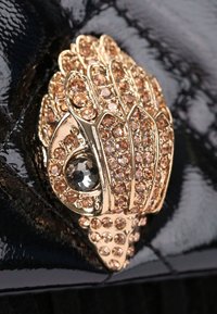 Złote metalowe akcesoria w kształcie dłoni, ozdobione przejrzystymi i różowymi cyrkoniami, na czarnym błyszczącym tle.