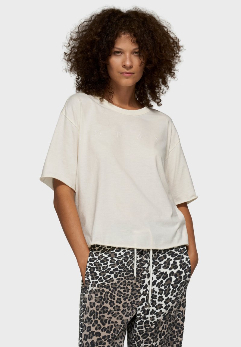 Camiseta de manga corta color crema con cuello redondo y diseño de texto sutil, combinada con pantalones jogger beige de estampado de leopardo y cintura con cordón.