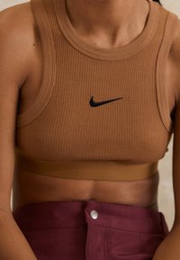 Brun ribbad sportbh med en svart Nike-logotyp. Designen har en rund halsringning och en solid nederdel.