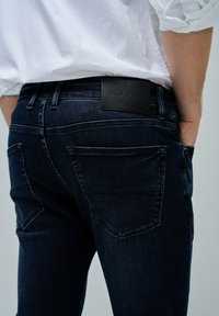 Vaqueros de mezclilla azul oscuro con una textura suave, con bolsillos traseros y una etiqueta de cuero negro grabada con "Salsa Jeans."