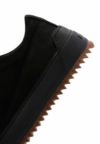 Sneaker nera con tomaia in pelle liscia, dettagli in gomma testurizzata e suola a zig zag con una finitura traslucida marrone.