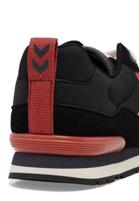 Czarne sneakersy z teksturowaną cholewką, czerwoną pętelką na pięcie z wzorem chevron oraz gumową podeszwą z białą i czarną obwódką.