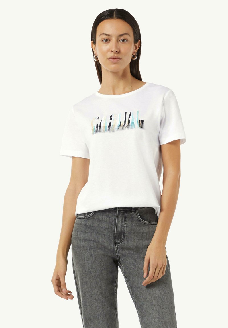 Weißes Baumwoll-T-Shirt mit kurzen Ärmeln, ausgestattet mit einem bunten "CASUAL" Grafikdruck. Getragen mit grauen Jeans.