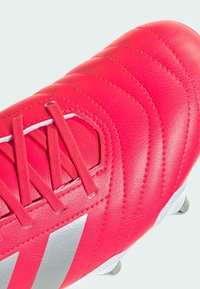 Scarpa da calcio sintetica rossa con upper in pelle texturizzata, dettagli cuciti, logo argentato e design con lacci, dotata di tacchetti conici sulla suola.