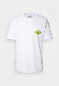 Valkoinen puuvillapaita, jossa on pieni, värikäs kukkakuva vasemmassa rintataskualueessa, pyöreä kaula-aukko ja lyhyet hihat.