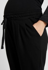 Svarta gravidybyxor med elastisk midja och dragsko, plisserad front och sidofickor. Mjuk tyg med slät textur.