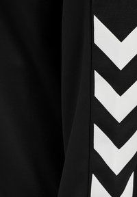 Schwarzer Sportstoff mit einem markanten weißen Chevron-Muster an einer Seite, das eine strukturierte Oberfläche und saubere Linien zeigt.