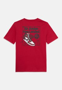 T-shirt en coton rouge avec un imprimé graphique d'une chaussure Air Jordan et le texte "Air Jordan a atterri" ainsi que des détails sur le cuir.
