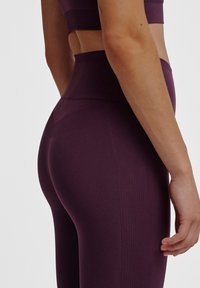 Hoch taillierte Leggings aus tiefviolettem Stoff, mit einem strukturierten Muster und nahtlosem Design, das an den Seiten eine glatte Oberfläche aufweist.