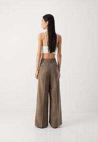 Hnedé široké nohavice vyrobené z textúrovanej látky, s funkčnými zadnými vreckami a vysokým pásom. Modelka má na sebe biely crop top.