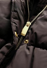 Schwarze Pufferjacke mit goldener Reißverschluss und Druckknöpfen, glatter, glänzender Textur und gerafftem Nähten für Isolierung und Stil.
