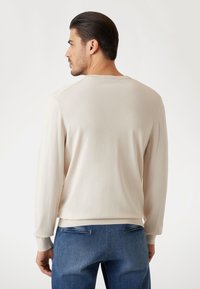 Felpa a maniche lunghe di un leggero color beige, con polsini e orlo a coste. Tessuto morbido, scollatura rotonda e dettagli di cucitura minimi. Abbinata a jeans blu.