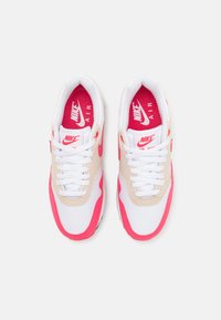 Sapatilhas Nike Air Max com parte superior em malha branca, detalhes em camurça rosa e palmilhas com a marca em vermelho. Os atacadores são brancos. A sola é preta.