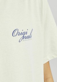 Gaiši zaļš kokvilnas T-krekls ar tumši zilu "Originals Worldwide" logo dizainu kreisajā krūtī. Īsas piedurknes, brīva piegriezuma.
